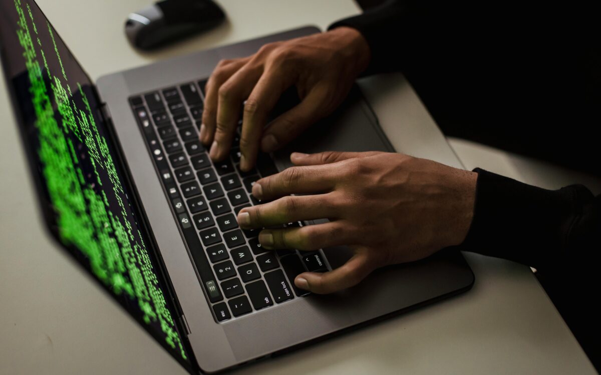 From above of crop anonymous male hacker typing on netbook with data on screen while sitting at desk